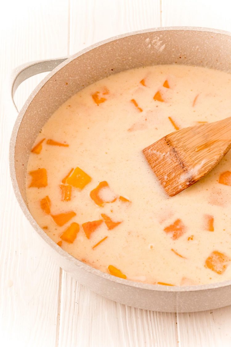butternut squash cubes, broth, milk, and cream with spices cooking in a tan skillet.