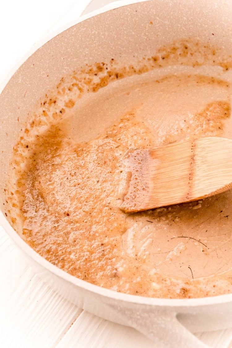 Garlic and flour being cooked in a tan skillet.
