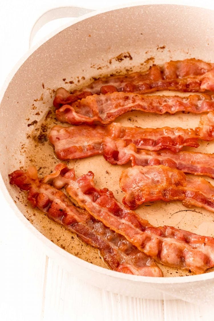 Bacon cooking in a tan skillet.