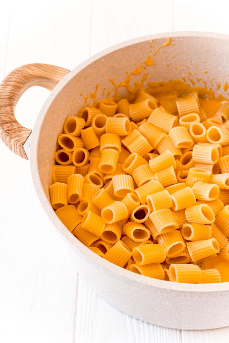 Pasta being added to a pot filled with butternut cream sauce.