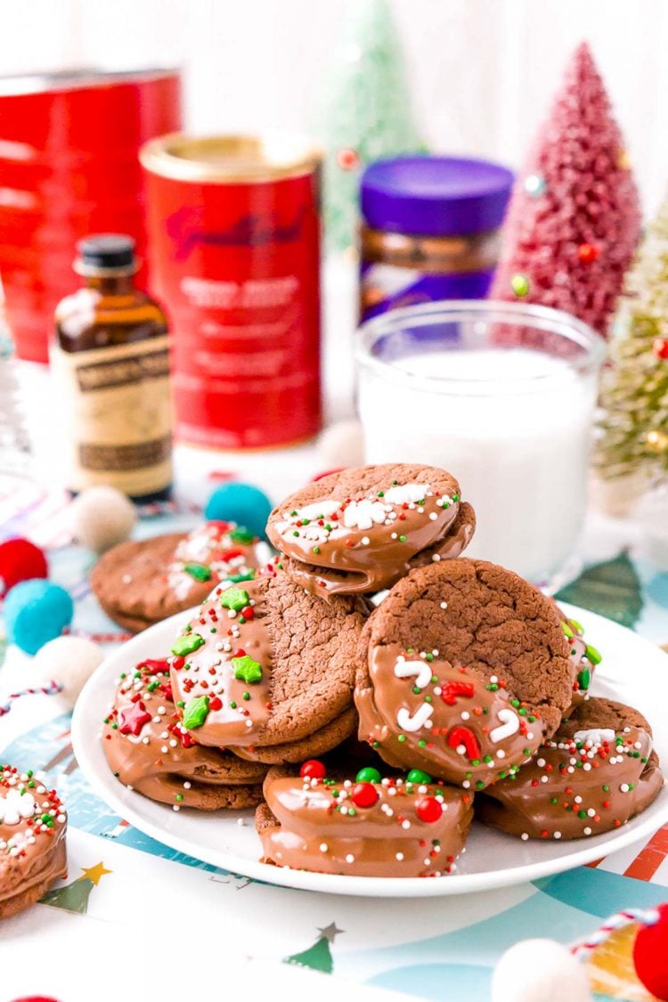 A plate of chocolate cookies decorated for the holidays with ingredients in the background.