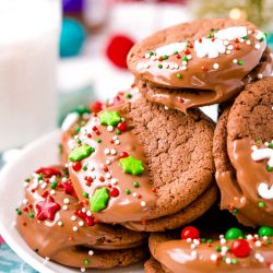 Close up photo of holiday decorated sandwich cookies on a white plate.