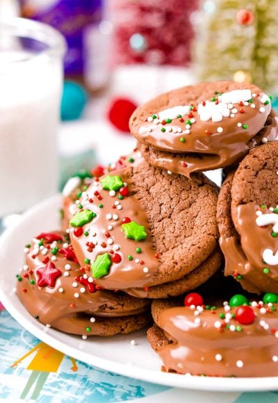 Close up photo of holiday decorated sandwich cookies on a white plate.