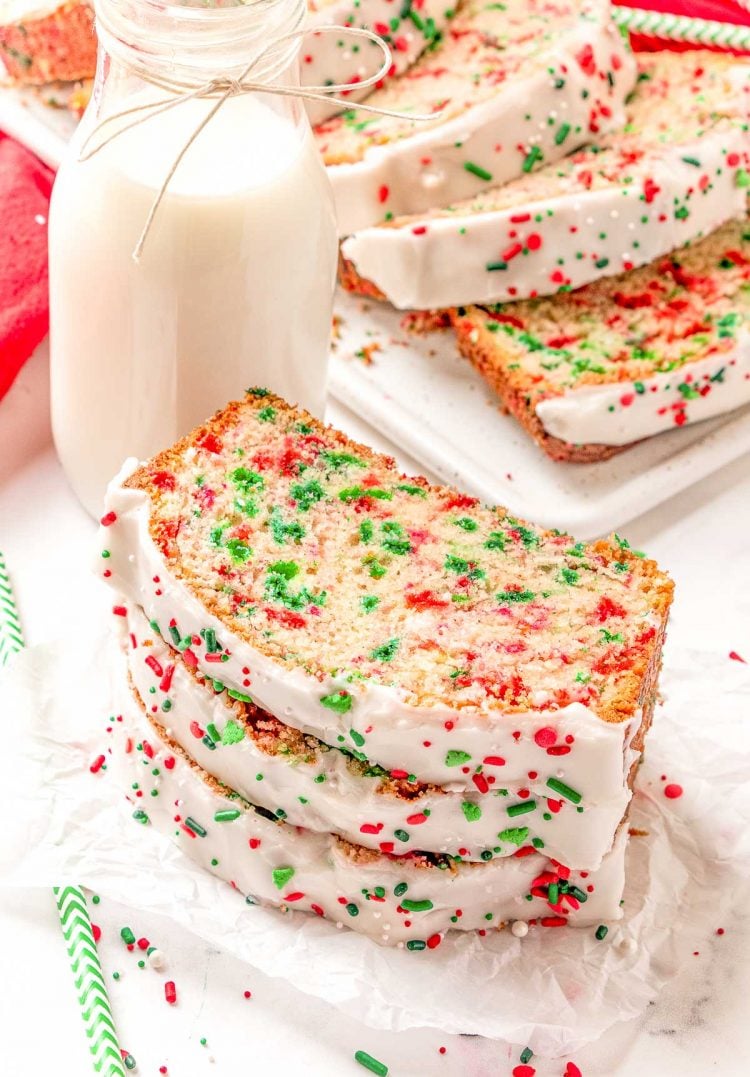 Slices of holiday quick bread on a table with a jug of milk and sprinkles.