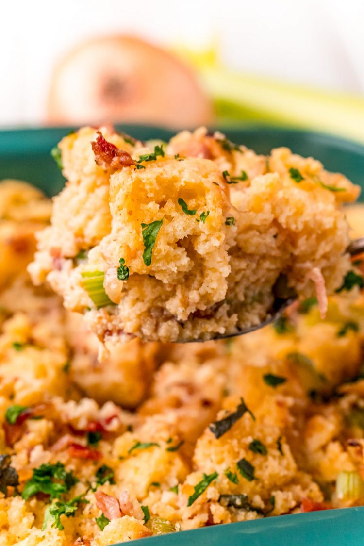 A serving spoon with a scoop of cornbread dressing over a baking dish.