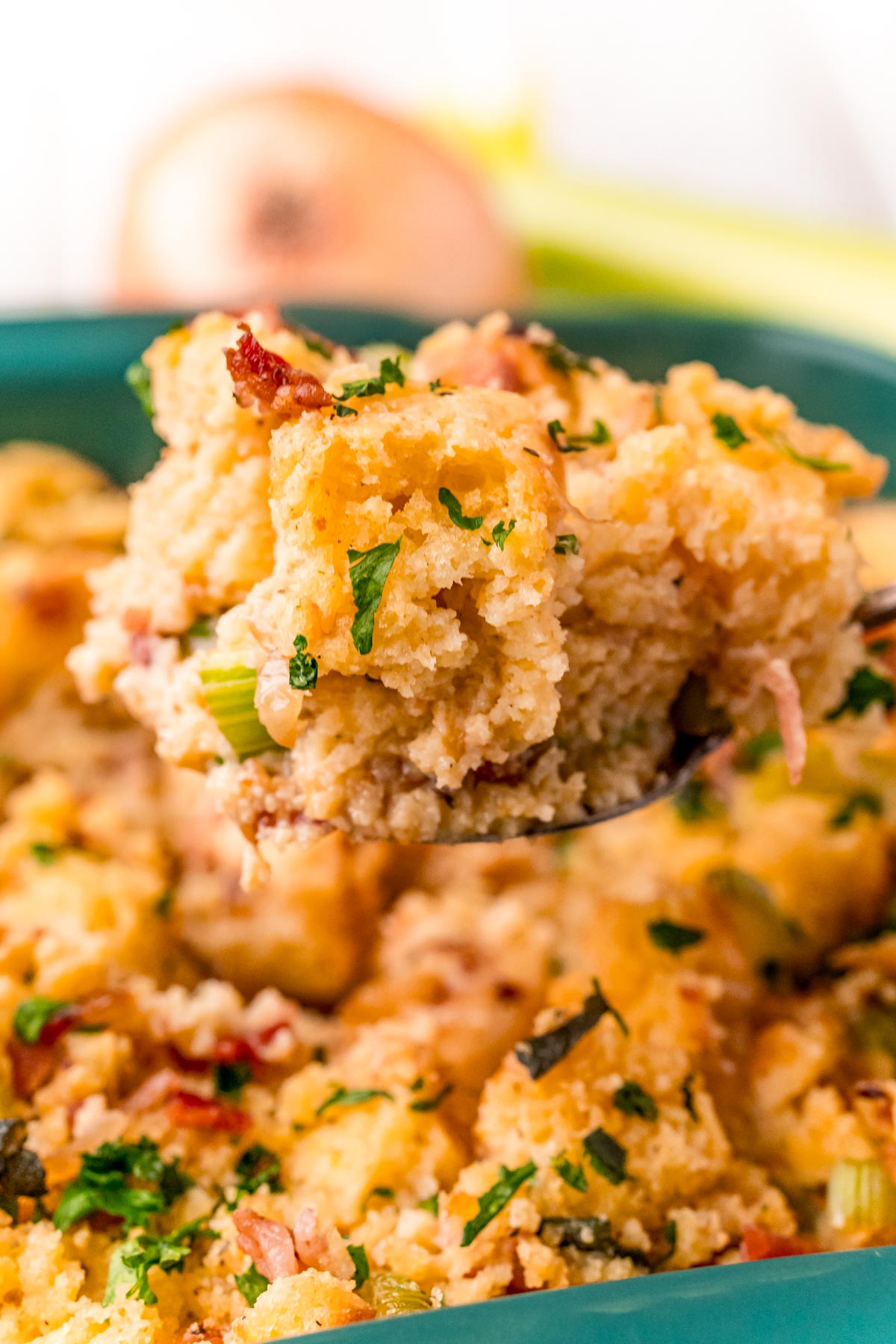 A serving spoon with a scoop of cornbread dressing over a baking dish.