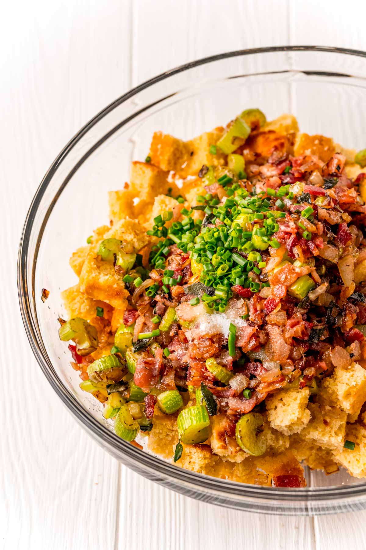 cornbread cubes, celery, onions, bacon, and chives in a glass mixing bowl.