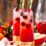 Close up photo of two fluted glasses filled with a red cocktail and cranberries.