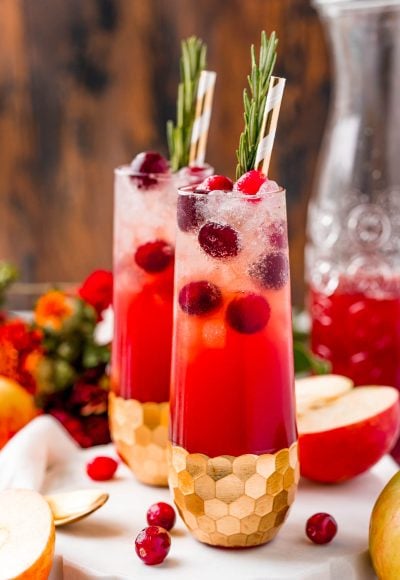 Close up photo of two fluted glasses filled with a red cocktail and cranberries.