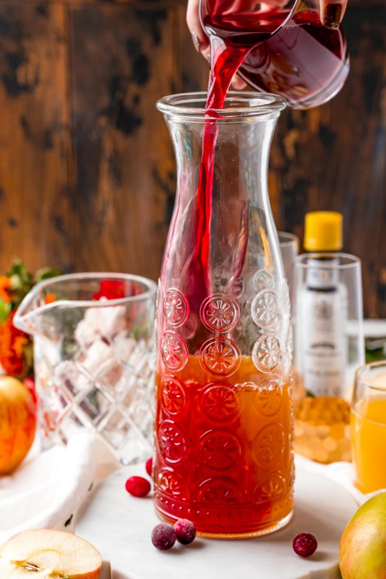 Cranberry juice being poured into a carafe to make a punch.