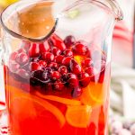 Close up photo of mimosa punch in a pitcher with cranberries.