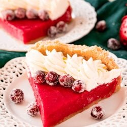 A slice of cranberry pie on a white plate topped with whipped cream and sugared cranberries.