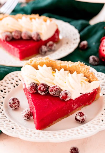 A slice of cranberry pie on a white plate topped with whipped cream and sugared cranberries.