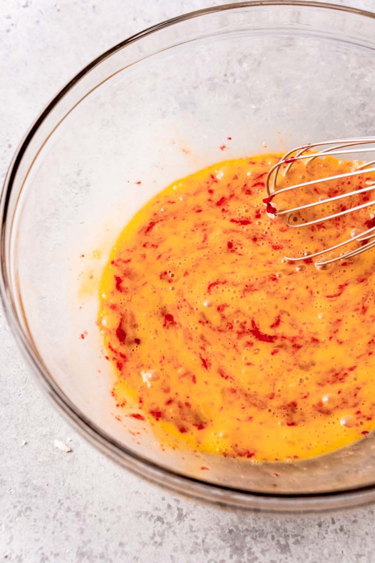 Beaten eggs in a glass mixing bowl with some cranberry curd mixed in.