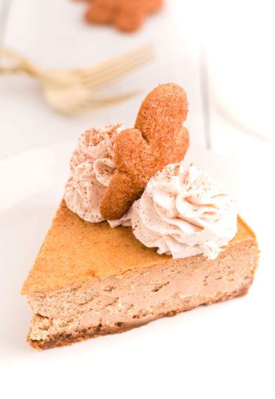 A slice of gingerbread cheesecake on a white plate with whipped cream and a gingerbread man on top.