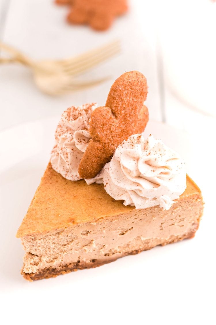 A slice of gingerbread cheesecake on a white plate with whipped cream and a gingerbread man on top.
