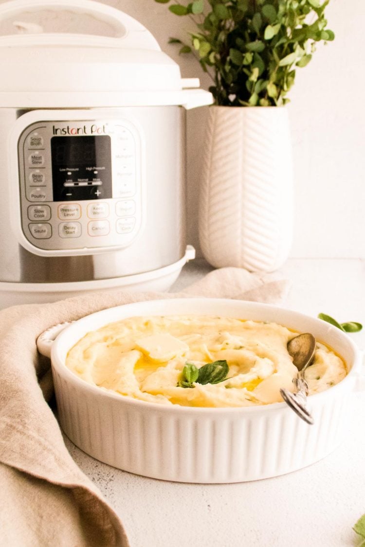 Mashed potatoes in a white serving dish with a white instant-pot and place in the background.