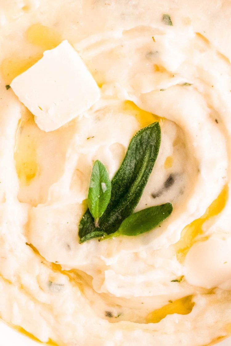 Super close up shot of mashed potatoes topped with butter and sage.