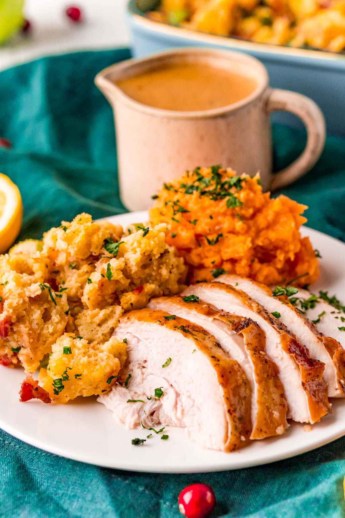 Close up photo of sliced turkey breast on a plate with mashed sweet potatoes and stuffing on the side.