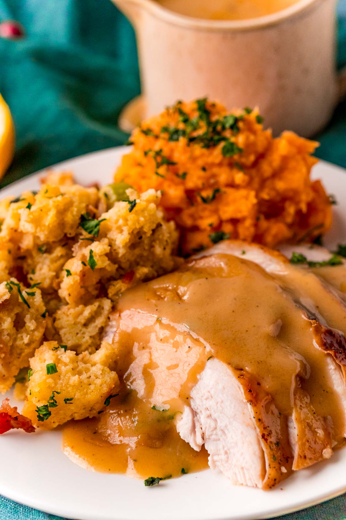 Sliced turkey breast with gravy on top and stuffing and sweet potatoes on the side.
