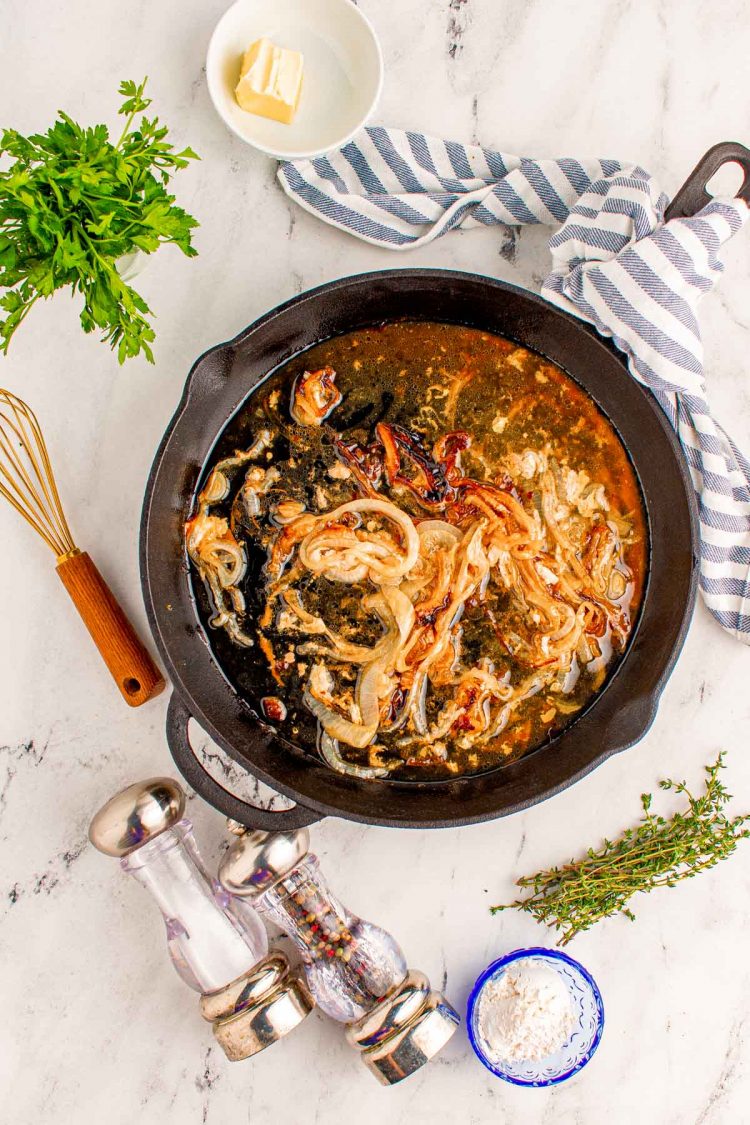 Overhead photo of caramelized onions in a cast iron skillet with other ingredients scattered around the pan.