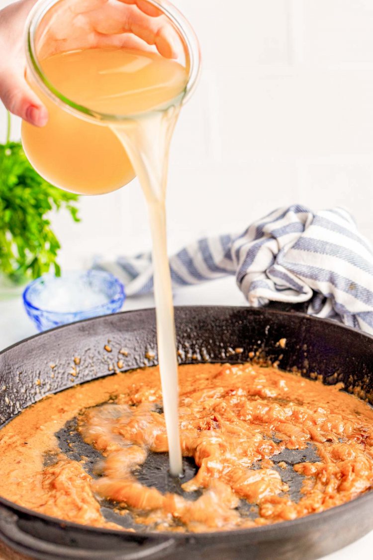 Chicken stock being poured into a cast iron skillet.