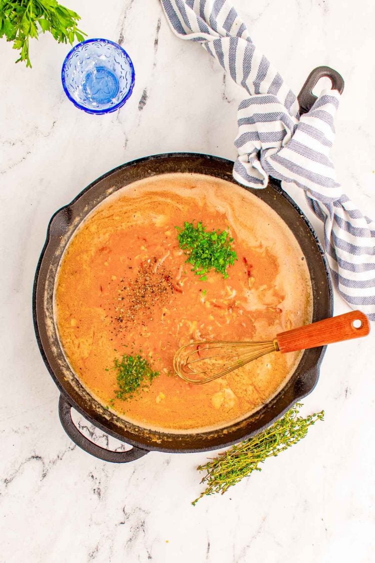 Overhead photo of onion gravy in a cast iron skillet with herbs and spices being added.