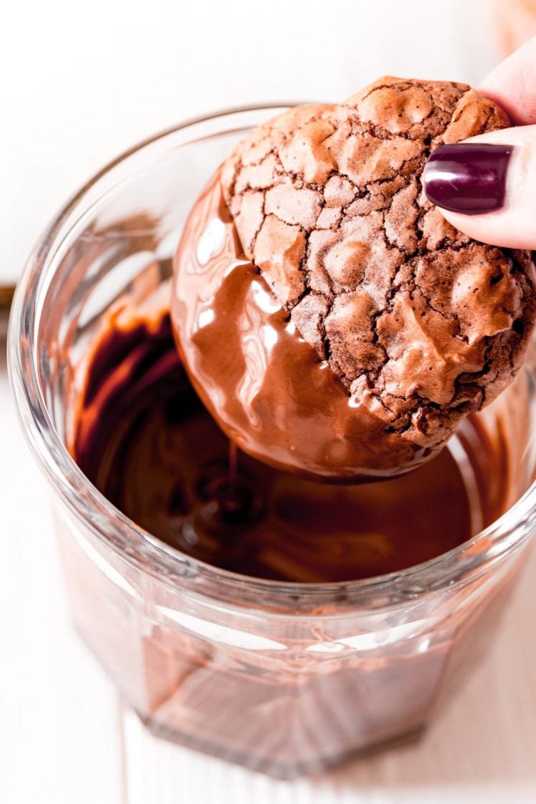 A woman's hand holding a brownie cookie and dipping it in chocolate.