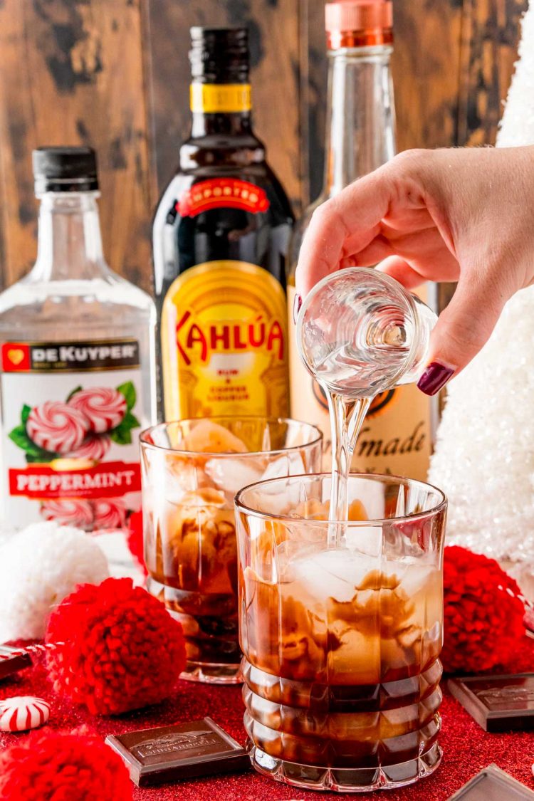 Vodka being poured into a rocks glass with chocolate, ice, and Kahlua.