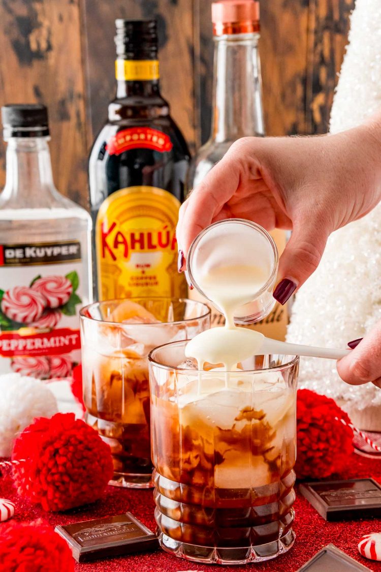 Heavy cream being poured over the back of a spoon into a rocks glass to make a white russian.