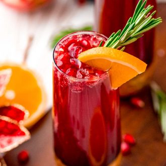 Close up photo of a pomegranate mimosa with orange and rosemary garnish.