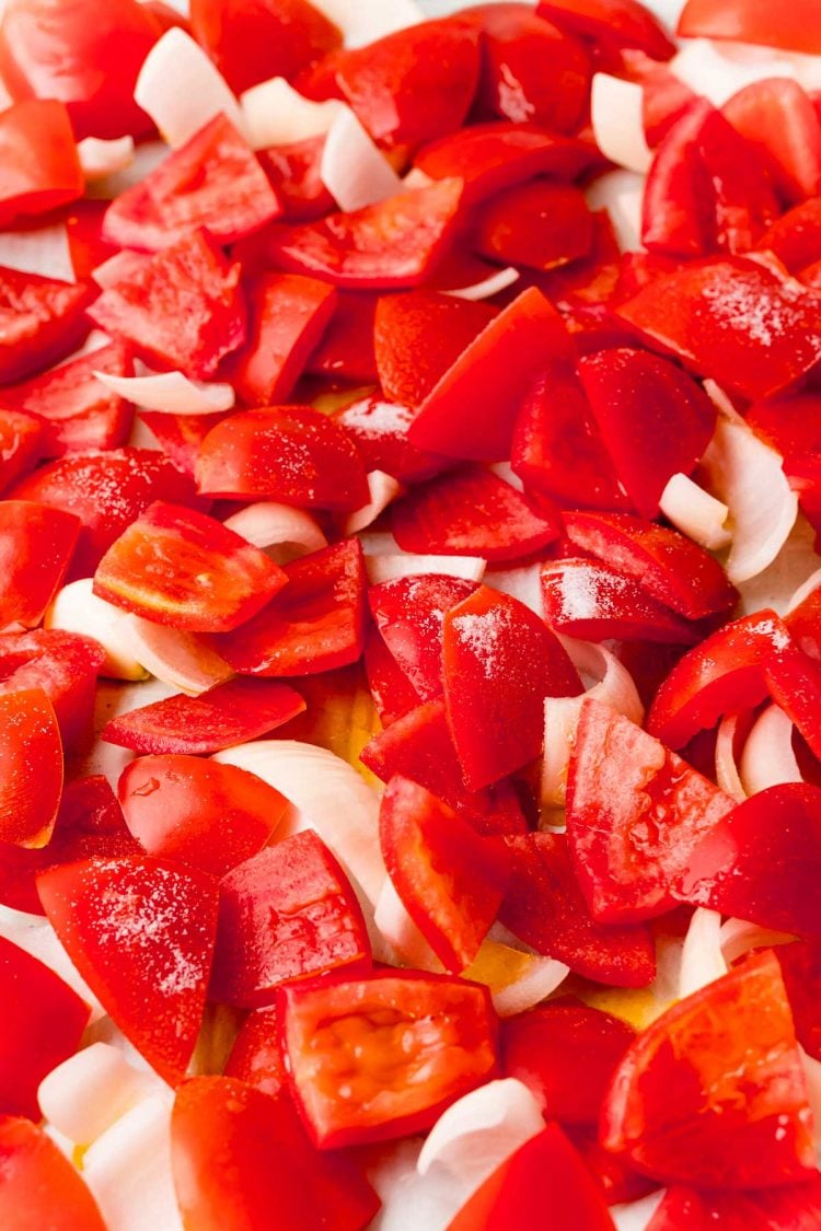 Close up photo of chopped tomatoes and onions on a baking sheet.