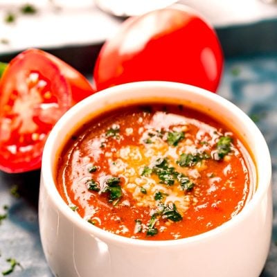 Close up photo of tomato soup in a white bowl topped with parmesan cheese and parsley.