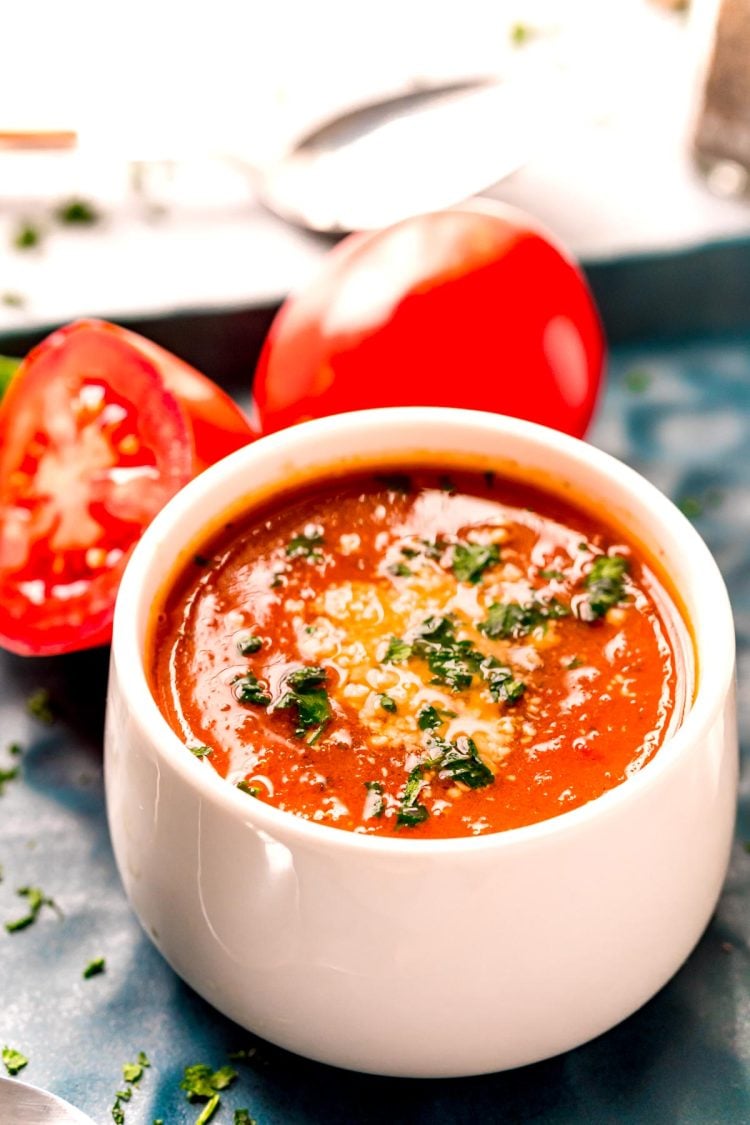 Close up photo of tomato soup in a white bowl topped with parmesan cheese and parsley.