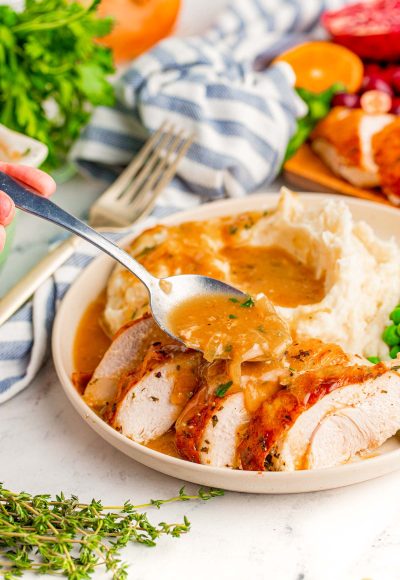 Onion gravy being spooned over a sliced turkey breast.