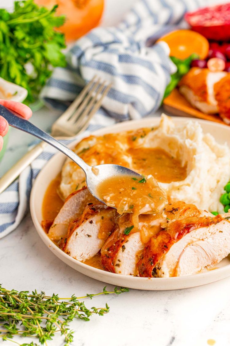 Onion gravy being spooned over a sliced turkey breast.