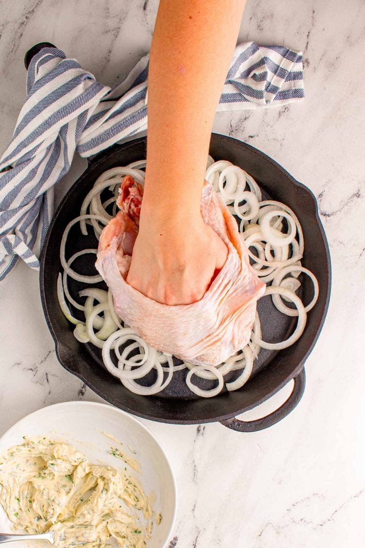 Overhead photo of a woman's hand separating turkey skin from the breast to apply herb butter underneath.