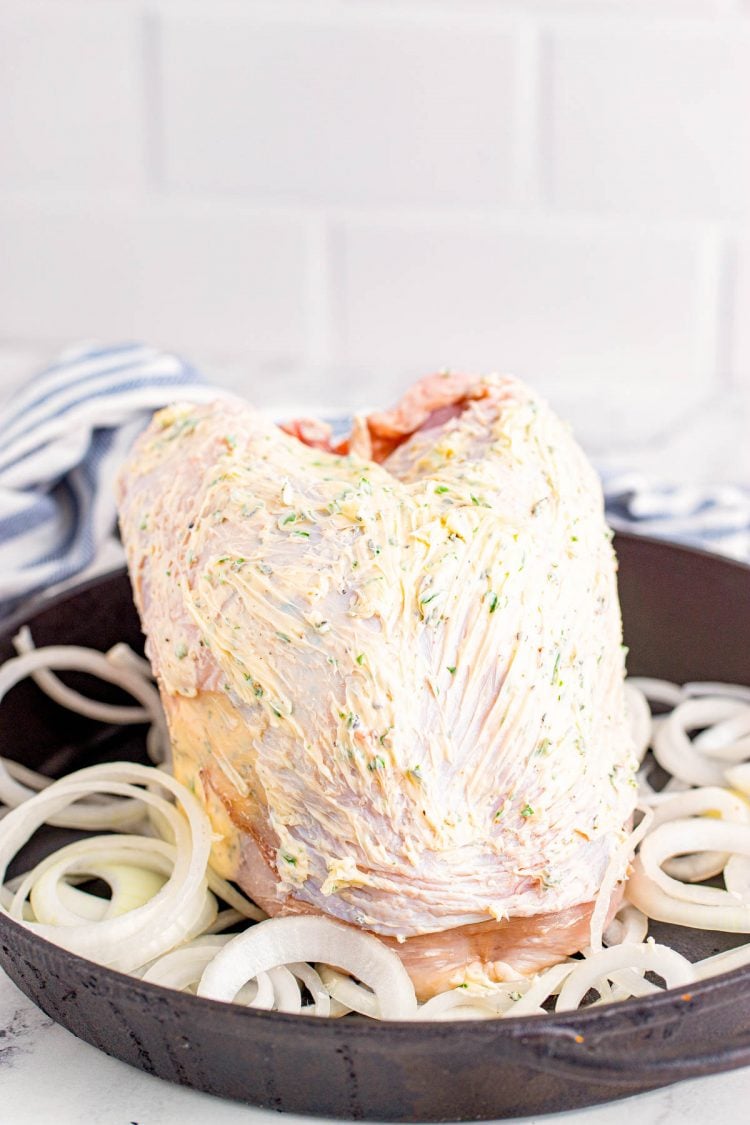 A turkey breast in a castiron skillet covered in herb butter.