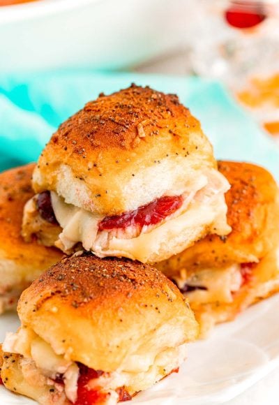 Close up photo of turkey sliders with cranberry sauce stacked on top of each other on a white plate.