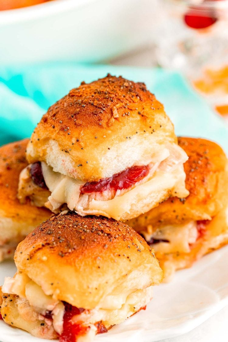 Close up photo of turkey sliders with cranberry sauce stacked on top of each other on a white plate.