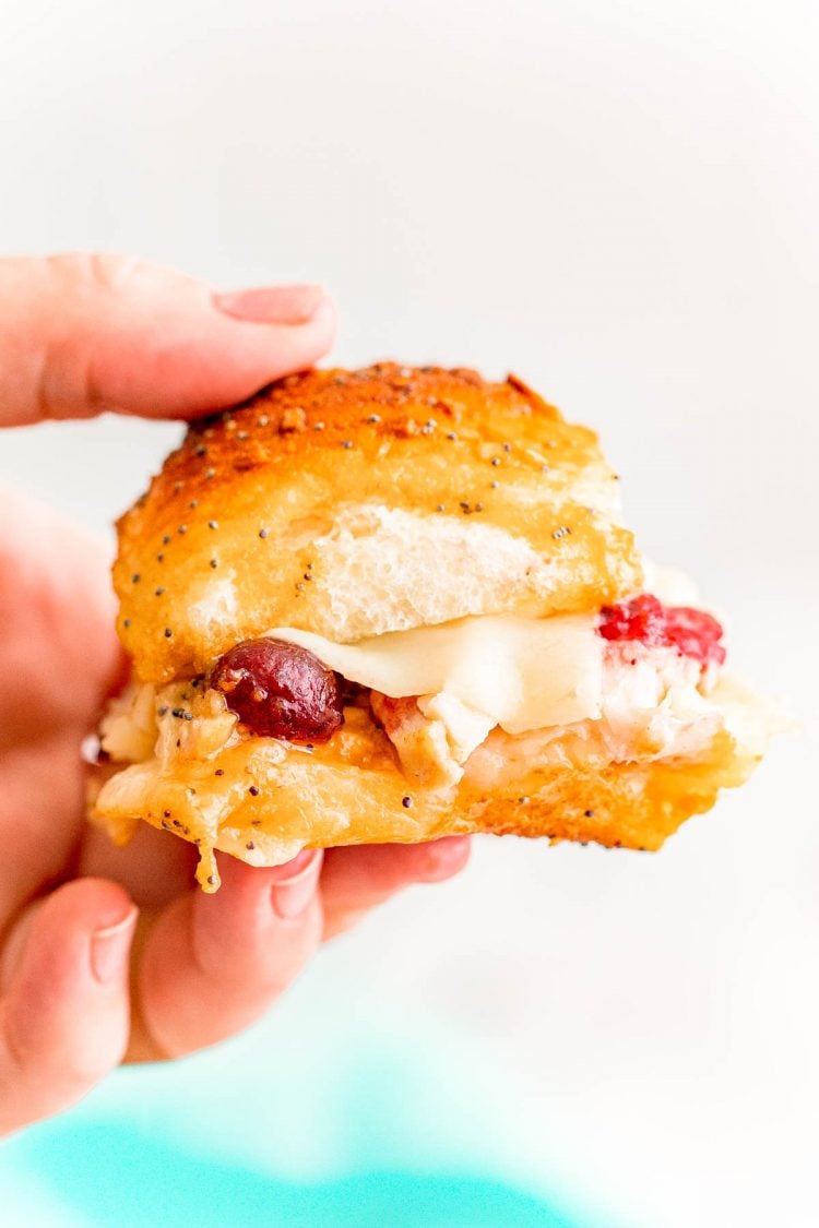 Close up photo of a woman's hand holding a turkey slider with cranberry sauce on it.