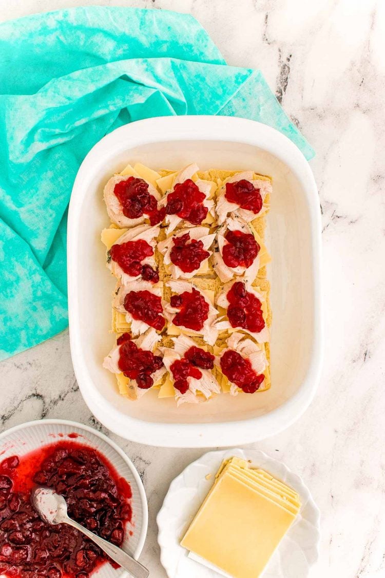 Overhead photo of thanksgiving sliders being prepared in a white casserole dish on a marble counter.