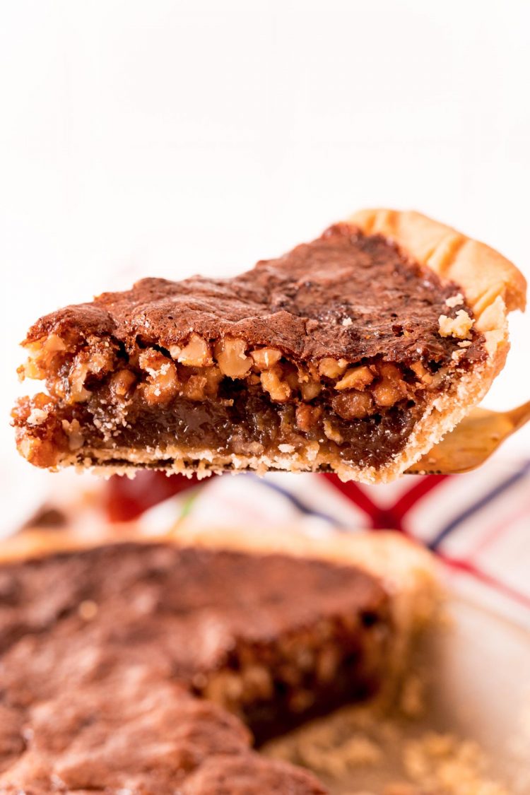 A piece of walnut pie being lifted away from the whole pie on a pie server.