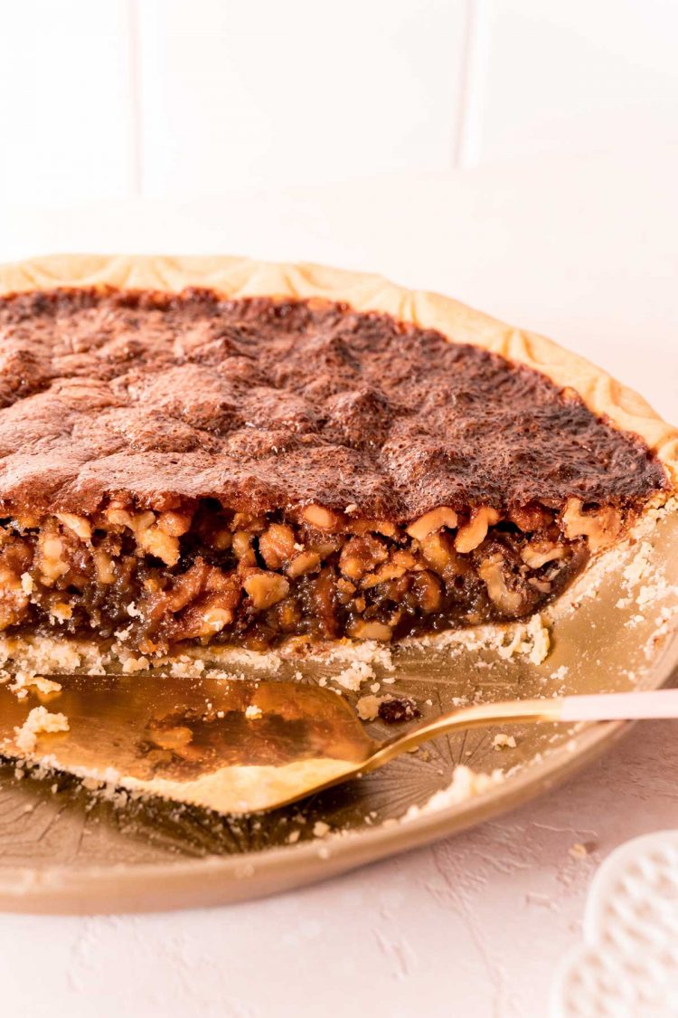 Half a walnut pie still sitting in the pan with a pie server.