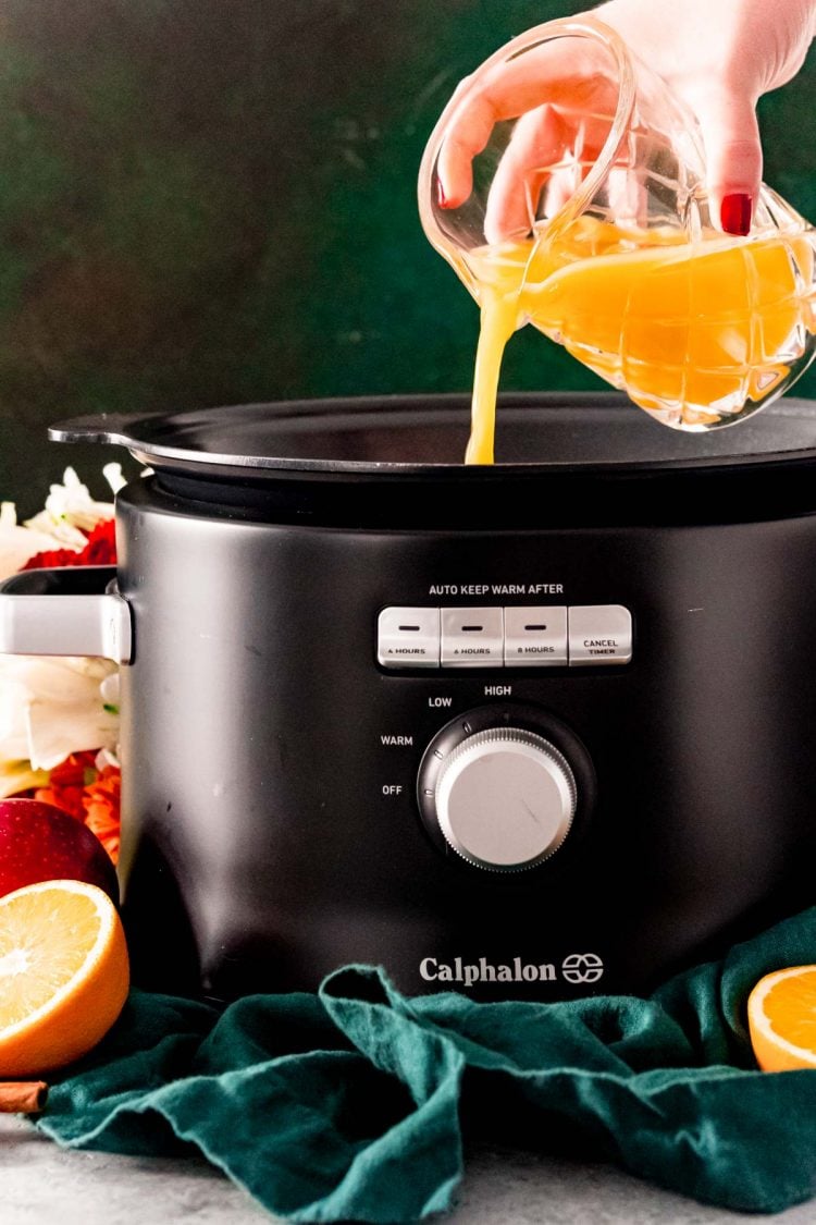 Orange juice being poured into a crock pot to make wassail.