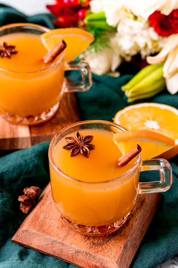 Two glass mugs of wassail on wooden coasters on a green napkin.