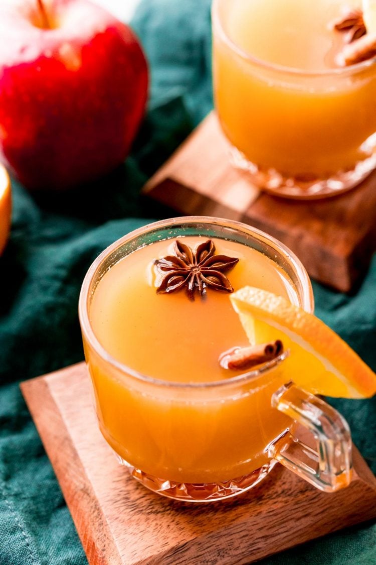 Foto de cerca de wassail en tazas de vidrio adornadas con palitos de canela y anís estrellado.