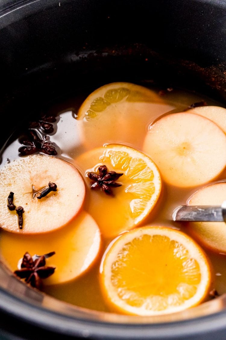 Wassail in a crockpot with sliced oranges and apples and star anise and cloves.
