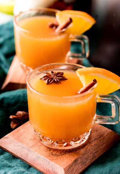 Close up photo of wassail in glass mugs garnished with cinnamon sticks and star anise.