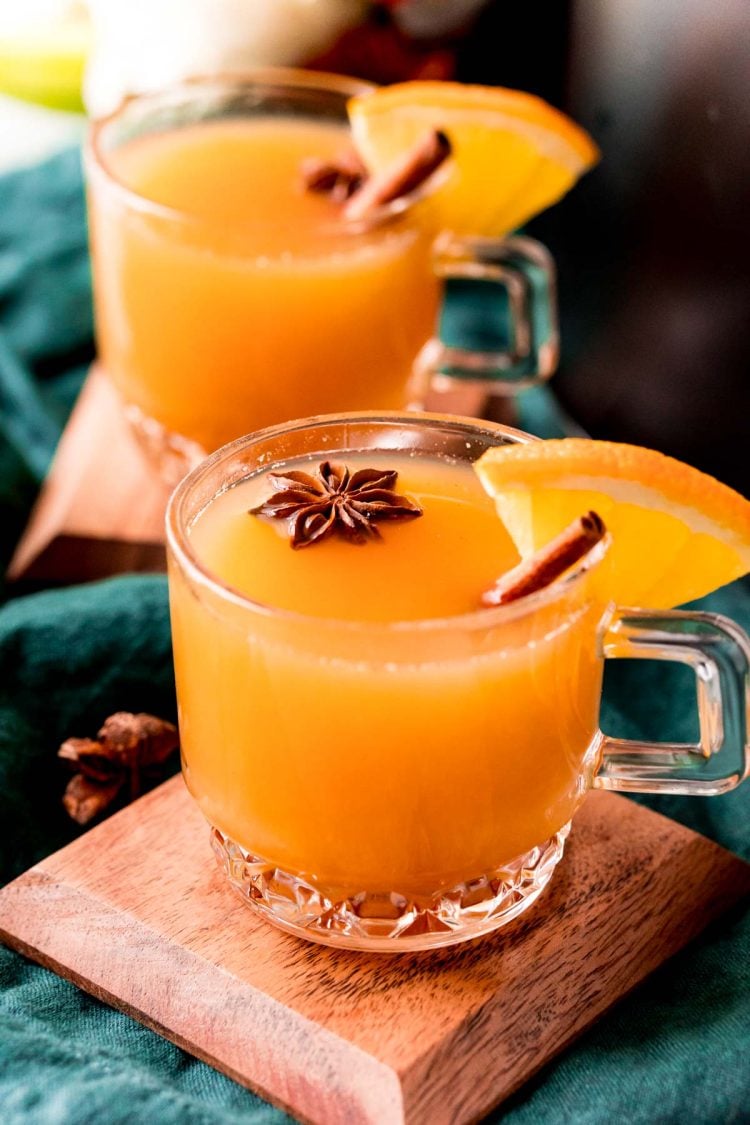 Close up photo of wassail in glass mugs garnished with cinnamon sticks and star anise.